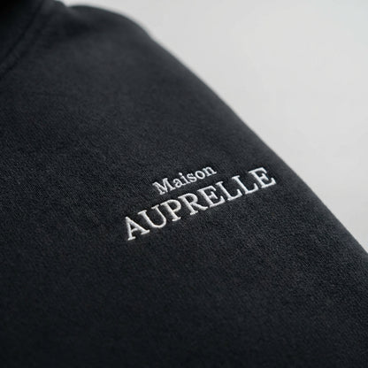 Black fabric with 'Maison Auprelle' embroidery on a gray background